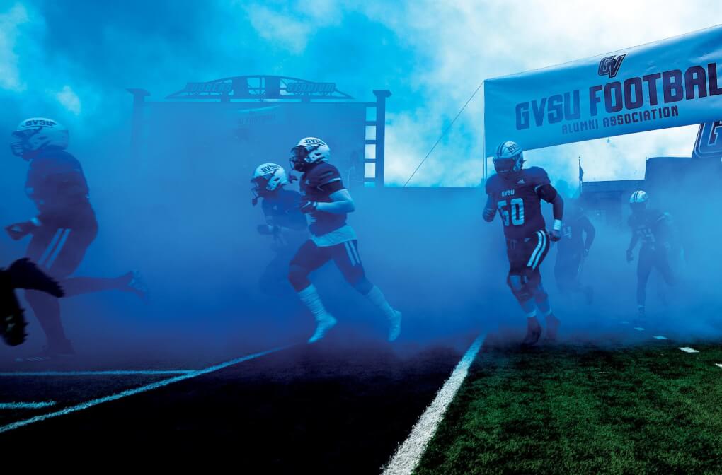 Football players running onto the football field in a cloud of blue
